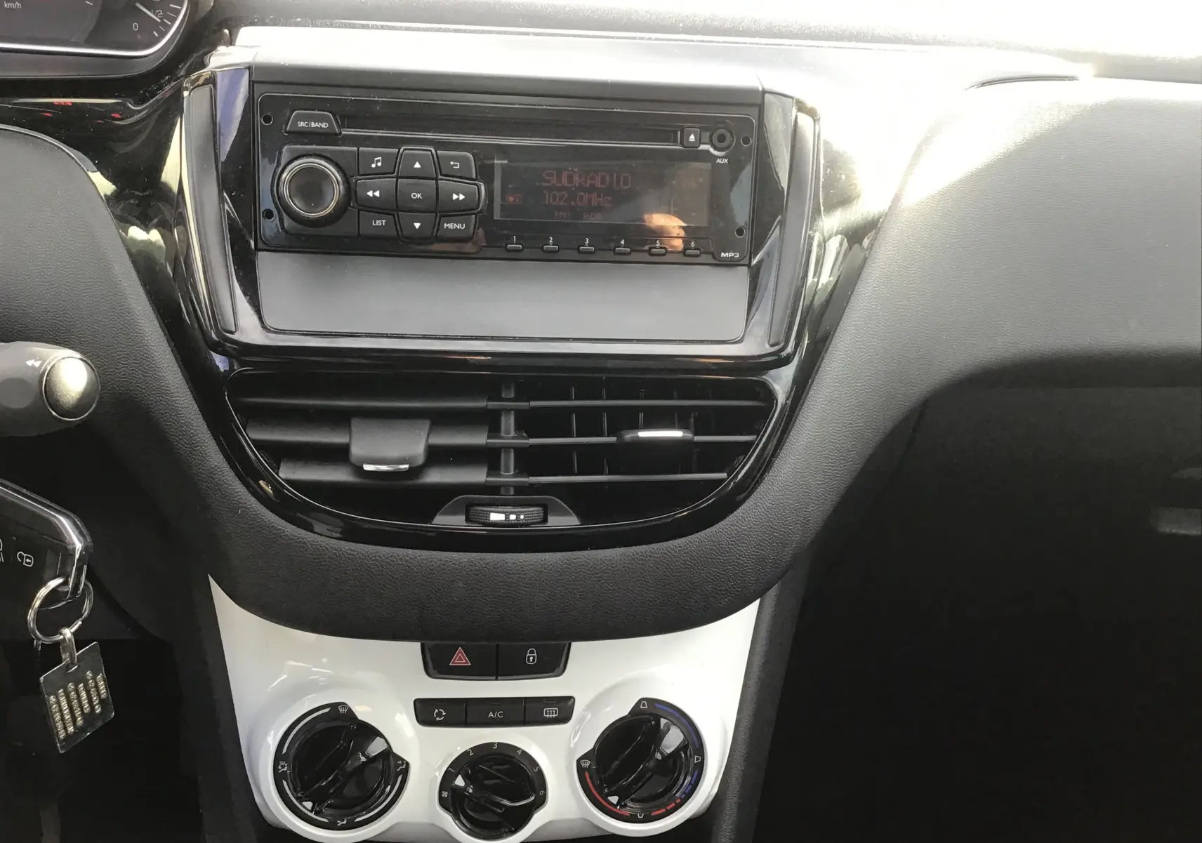 Vue rapprochée du tableau de bord noir et blanc de la Peugeot 208 1.2 PureTech 2018, avec radio et commandes de climatisation.