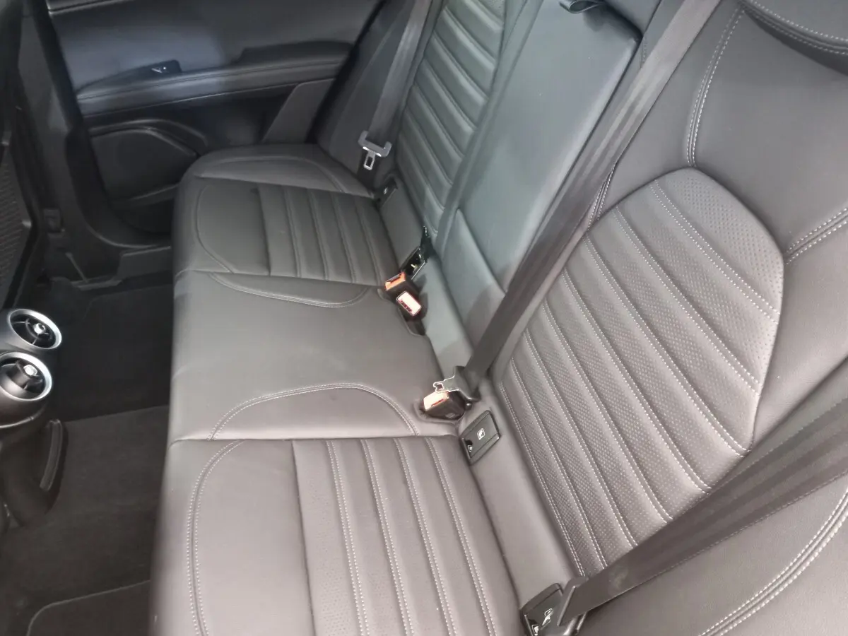 Vue intérieure sur la banquette arrière en cuir gris foncé de l'Alfa Romeo Stelvio 2024 avec ceintures et aérateurs.