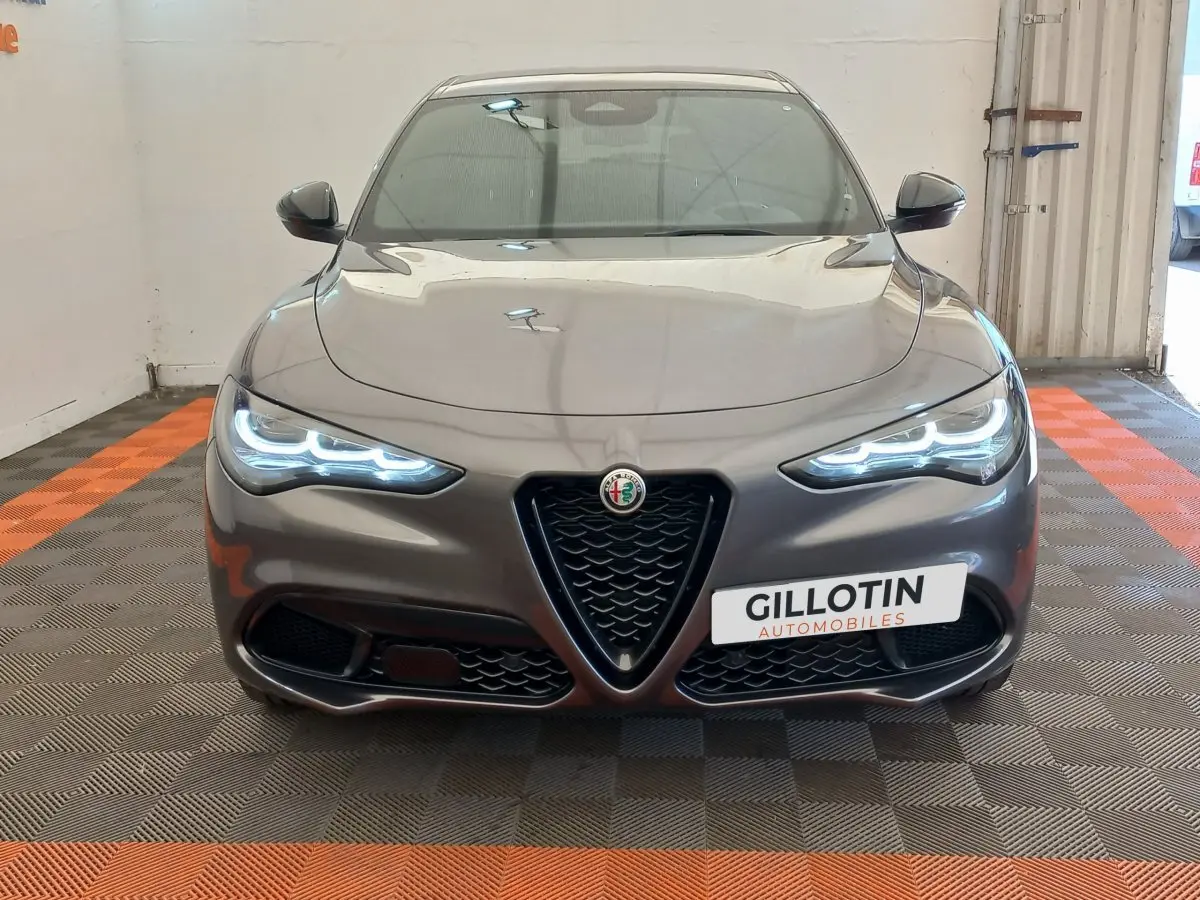 Vue frontale d'une Alfa Romeo Stelvio gris foncé 2024 avec phares LED allumés et calandre caractéristique en V.