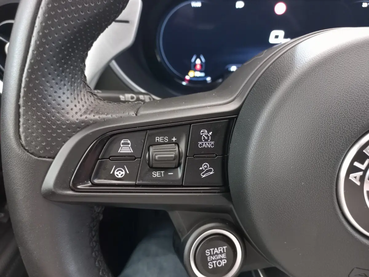 Gros plan sur les commandes multifonctions à gauche du volant cuir perforé de l'Alfa Romeo Stelvio 2024 avec bouton start/stop.