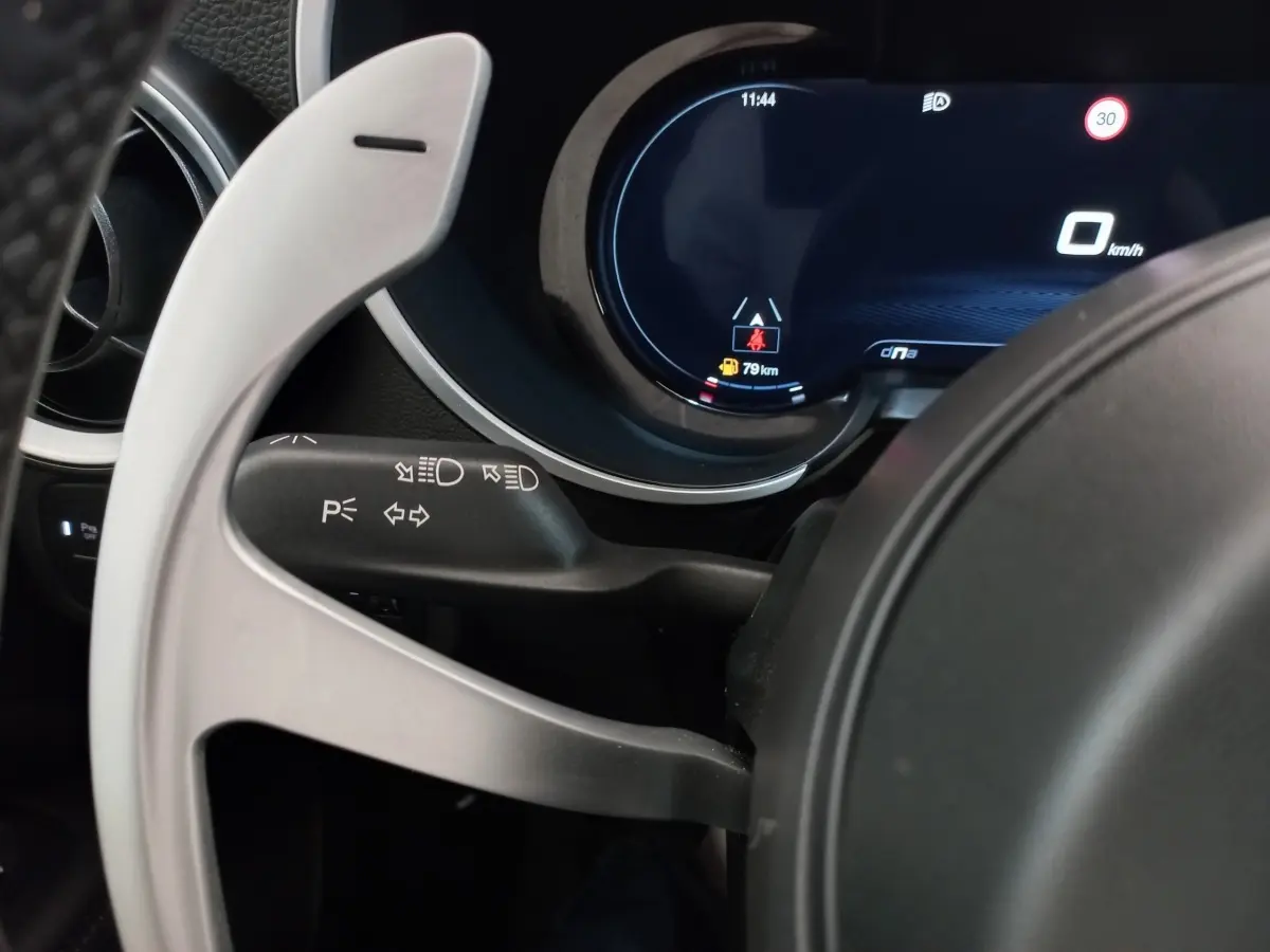 Gros plan sur le combiné d'instruments numérique et la palette de changement de vitesse alu du volant de l'Alfa Romeo Stelvio gris foncé.