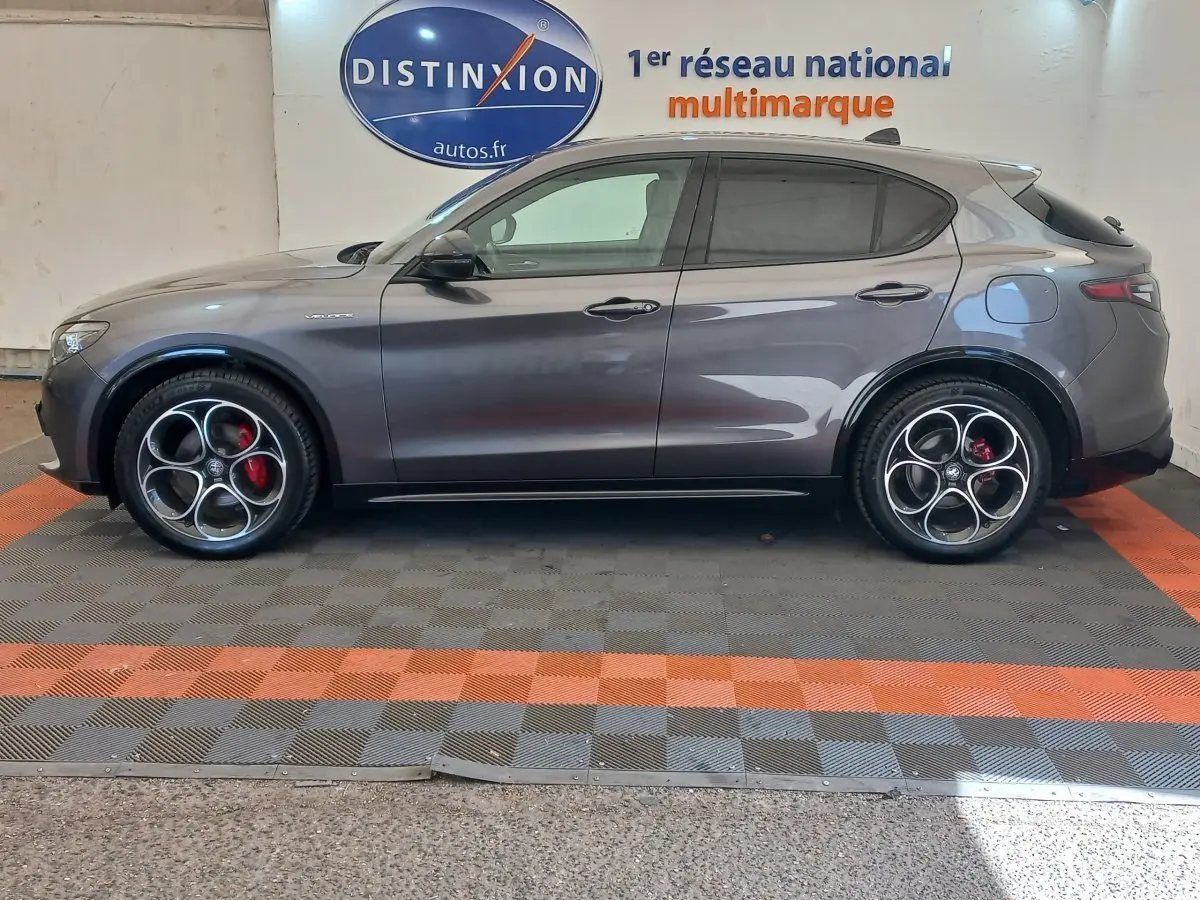 Vue de profil côté gauche d'un Alfa Romeo Stelvio gris foncé avec jantes sport et étriers rouges.