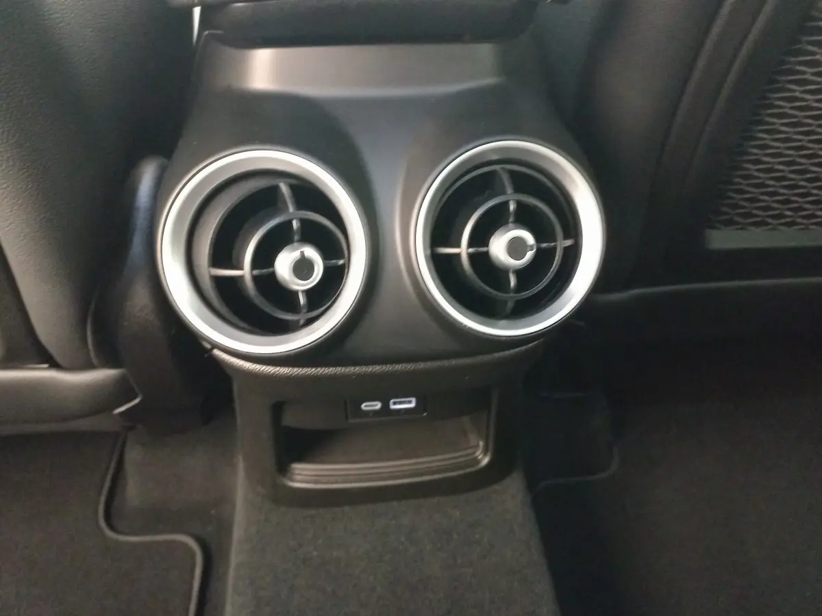 Détail des aérateurs arrière ronds avec bordure alu et prises USB dans l’habitacle noir de l’Alfa Romeo Stelvio 2024.