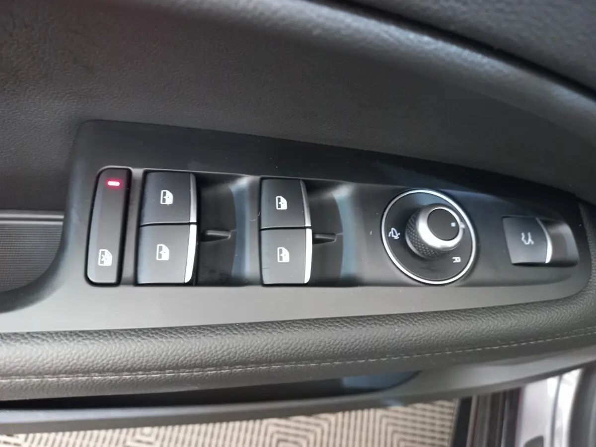 Gros plan sur les commandes de lève-vitres et rétroviseurs côté conducteur de l'Alfa Romeo Stelvio gris foncé.