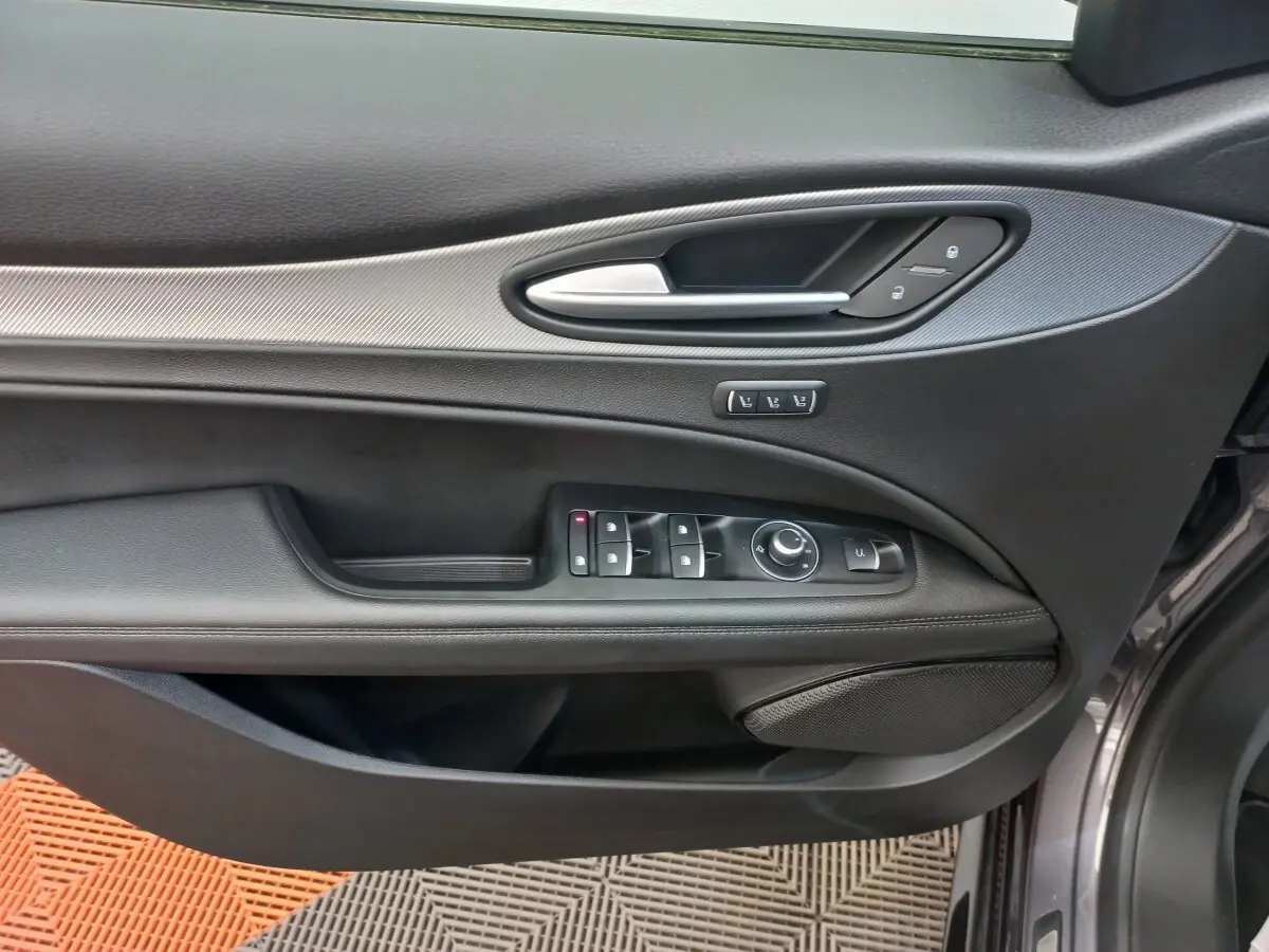 Gros plan sur la porte avant gauche gris foncé de l'Alfa Romeo Stelvio 2024 avec commandes électriques et poignée argentée.