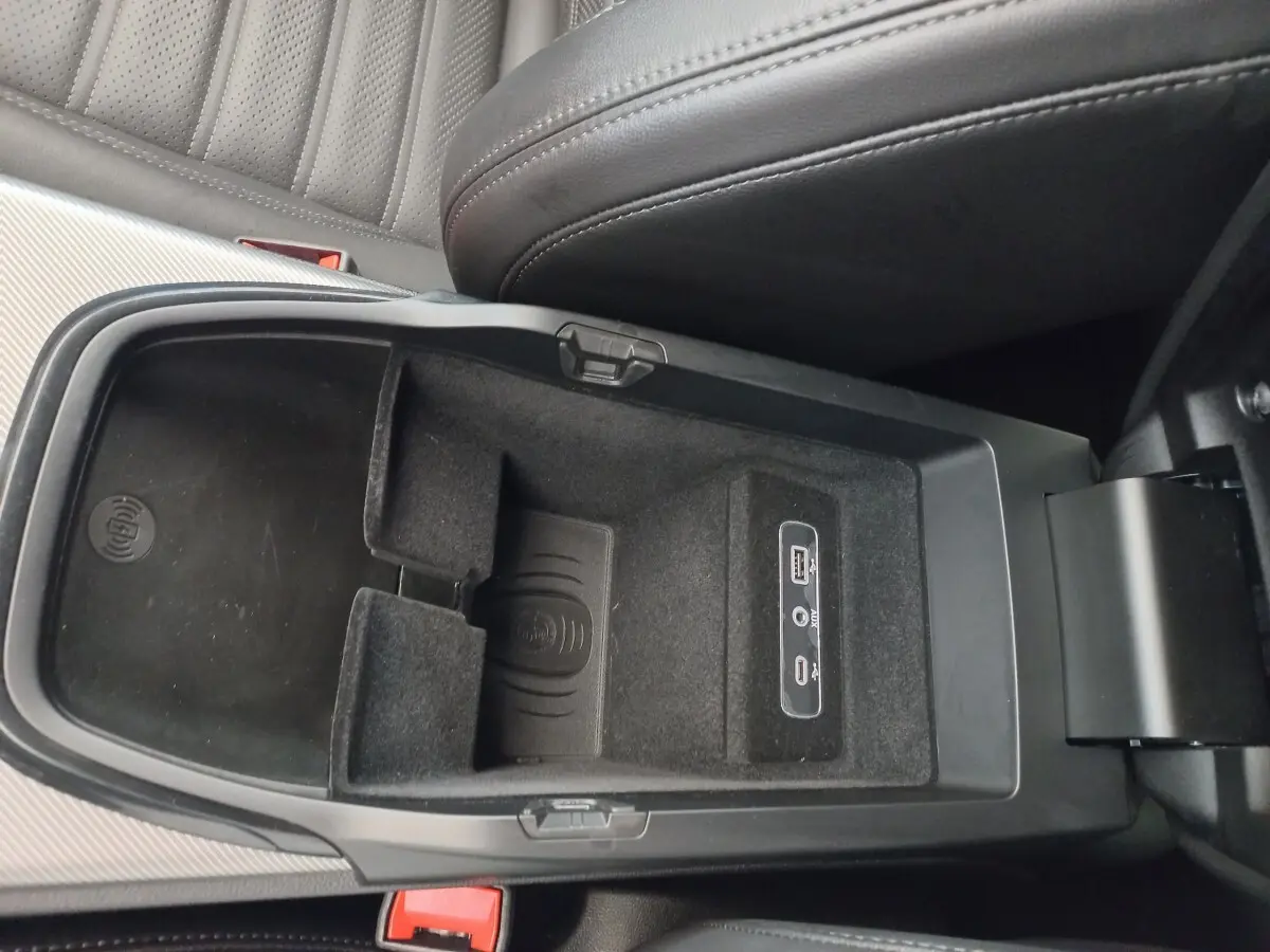 Vue intérieure du compartiment central ouvert de l'Alfa Romeo Stelvio gris foncé, montrant la zone de recharge par induction et ports USB.