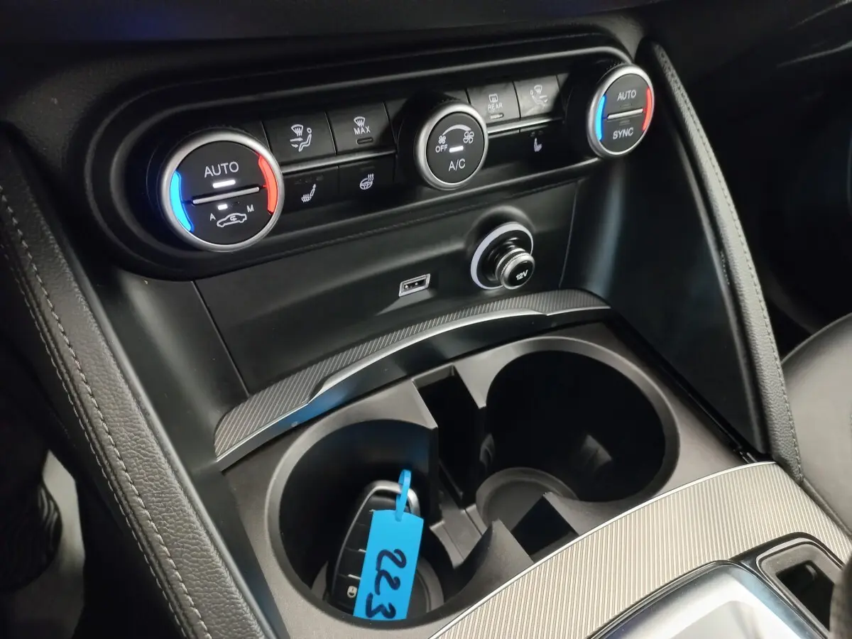 Gros plan sur la console centrale de l'Alfa Romeo Stelvio 2024, avec commandes climatisation et prise 12V visibles.