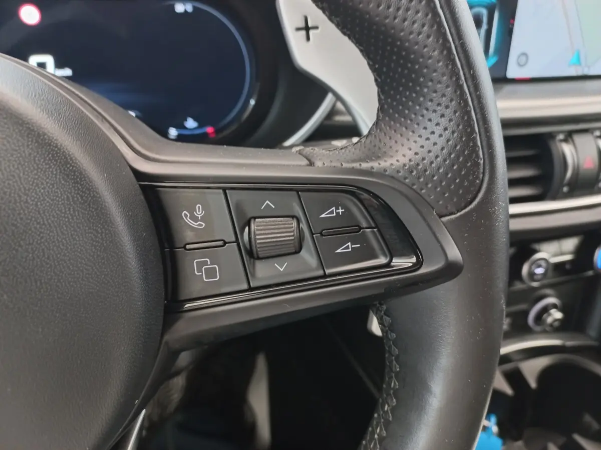 Gros plan sur les commandes du volant cuir perforé de l'Alfa Romeo Stelvio gris foncé, avec tableau de bord en arrière-plan.