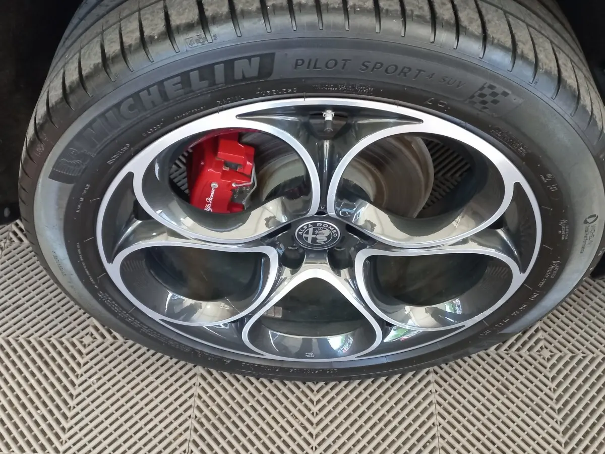 Gros plan sur la jante alu noire et argentée avec logo Alfa Romeo et étrier de frein rouge du Stelvio gris foncé.
