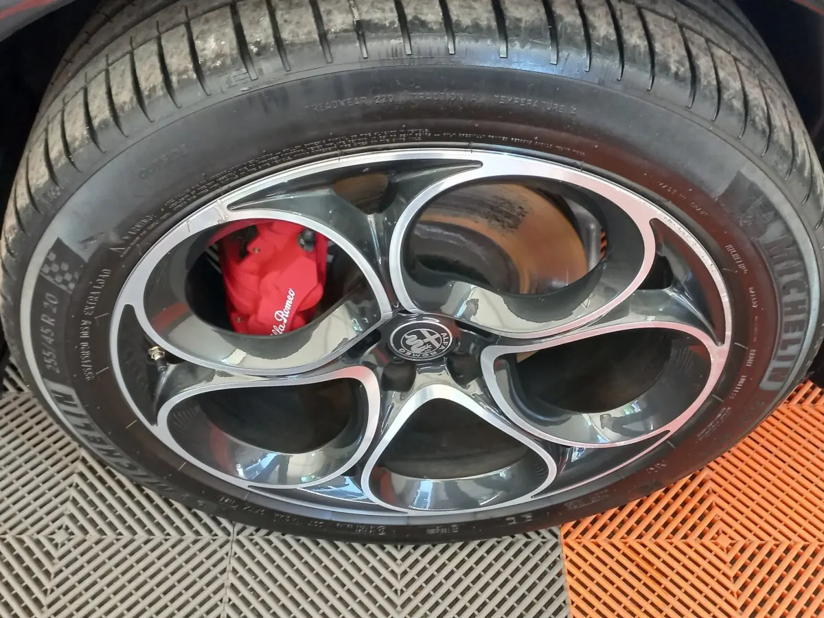 Gros plan sur la roue avant avec jante noire et argentée, étrier de frein rouge Alfa Romeo visible.