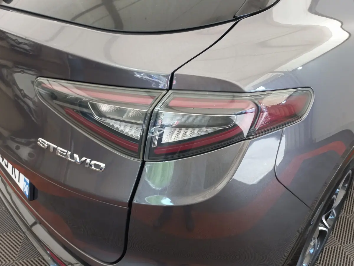 Gros plan sur le feu arrière droit et le logo Stelvio d’un Alfa Romeo gris foncé, vue arrière en légère plongée.