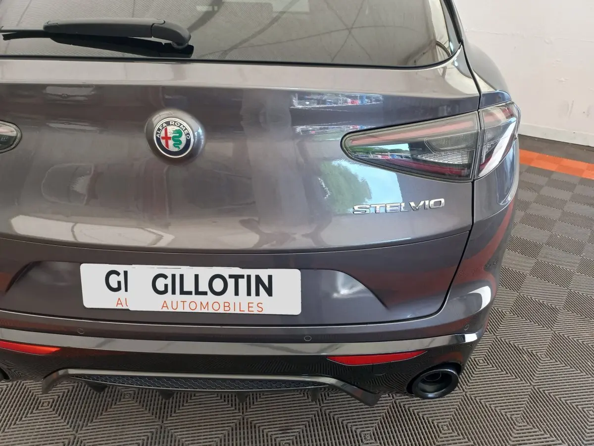 Vue arrière d'un Alfa Romeo Stelvio gris foncé avec logo central et feux arrière allongés, en intérieur showroom.