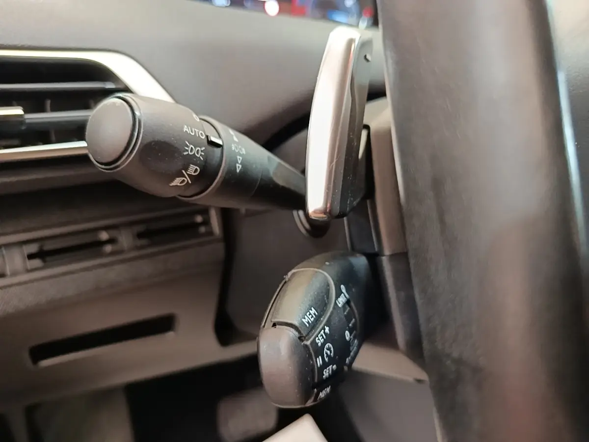 Gros plan sur les commandes au volant cuir noir du Peugeot 3008, avec levier de clignotants et régulateur de vitesse.