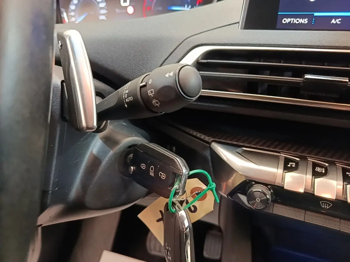 Gros plan sur le volant cuir et la clé insérée dans le contacteur d'une Peugeot 3008 noire, tableau de bord et commandes visibles.