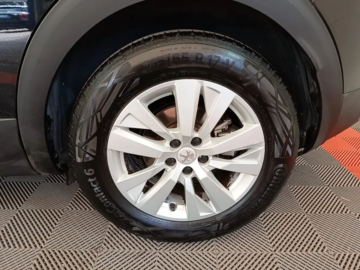 Gros plan sur la roue avant droite du Peugeot 3008 noir, mettant en valeur la jante alliage et le logo lion central.