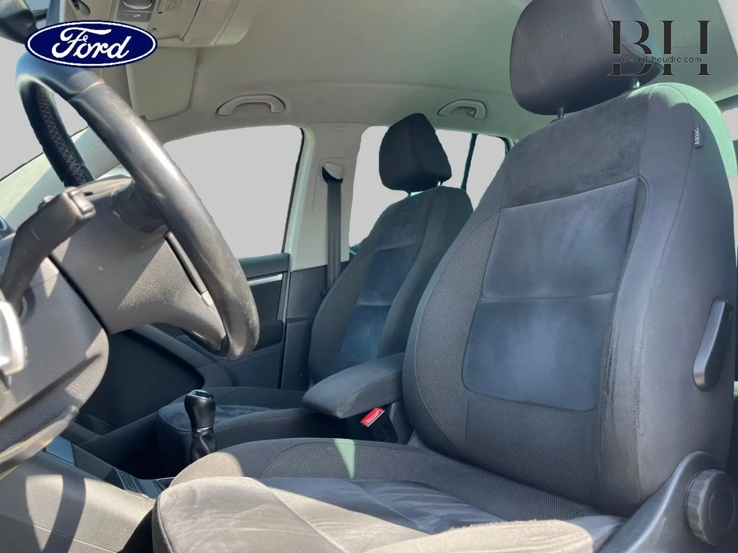 Vue intérieure côté conducteur montrant les sièges sport en tissu noir et alcantara avec accoudoir central.