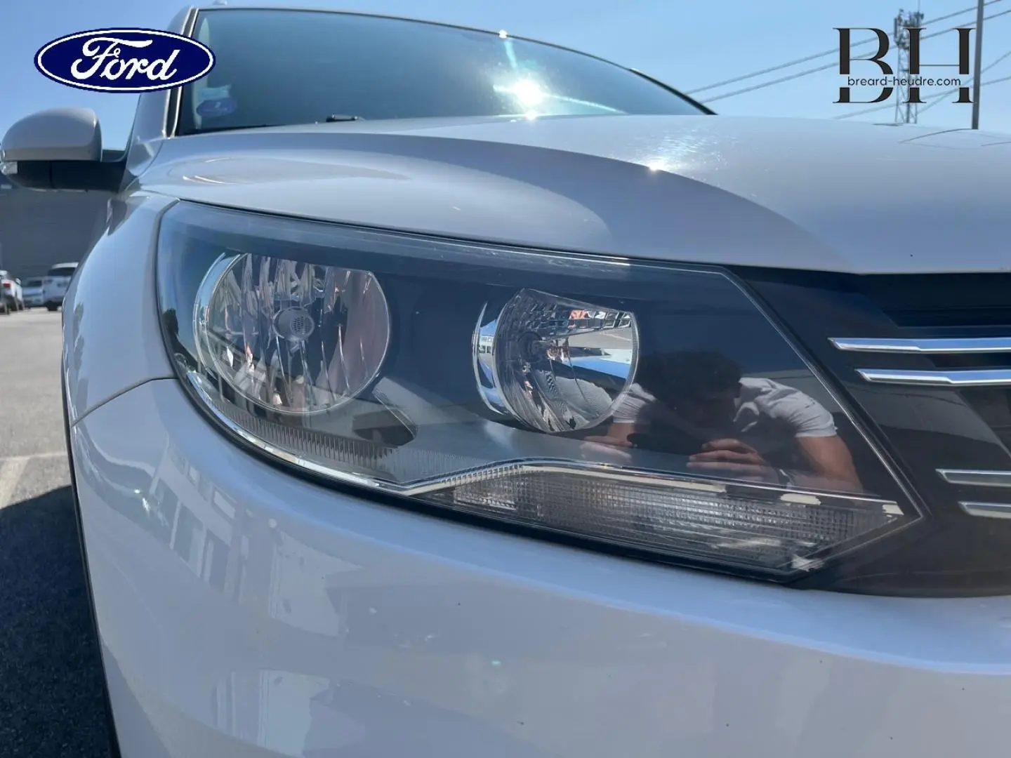 Gros plan sur le phare avant gauche d'un Volkswagen Tiguan blanc Candy, avec calandre noire et chrome visible.