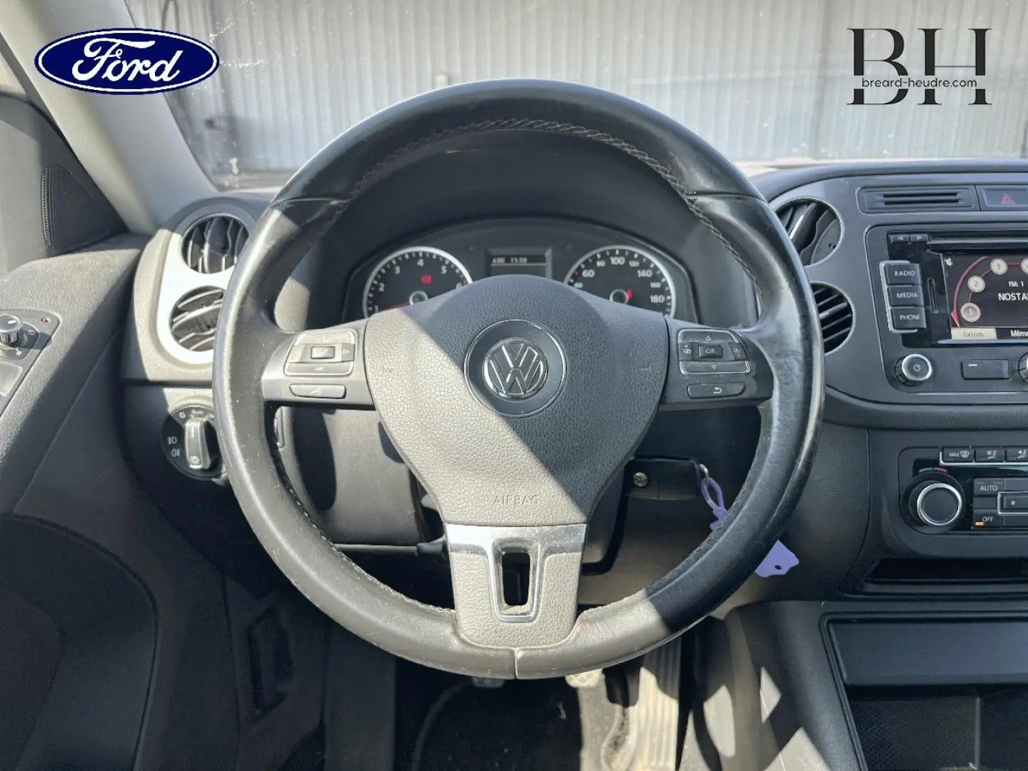 Vue intérieure centrée sur le volant cuir Volkswagen avec tableau de bord et écran tactile visibles.