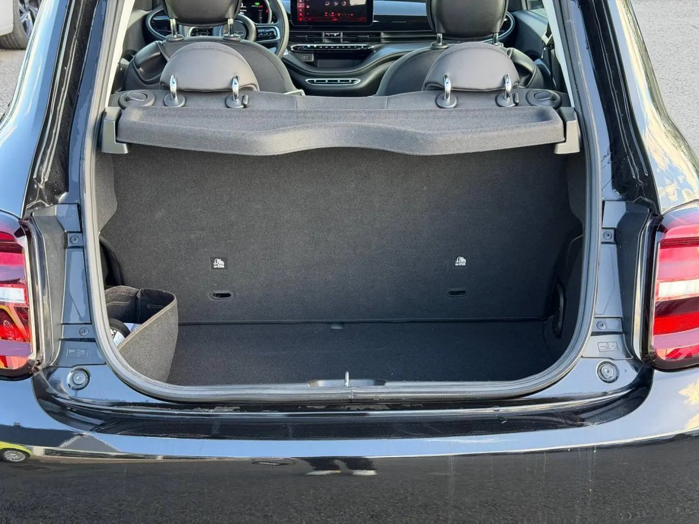 Coffre ouvert vu de l'arrière d'une Fiat 500 électrique 2024 Onyx Black pastel avec intérieur noir et tablette cache-bagages.