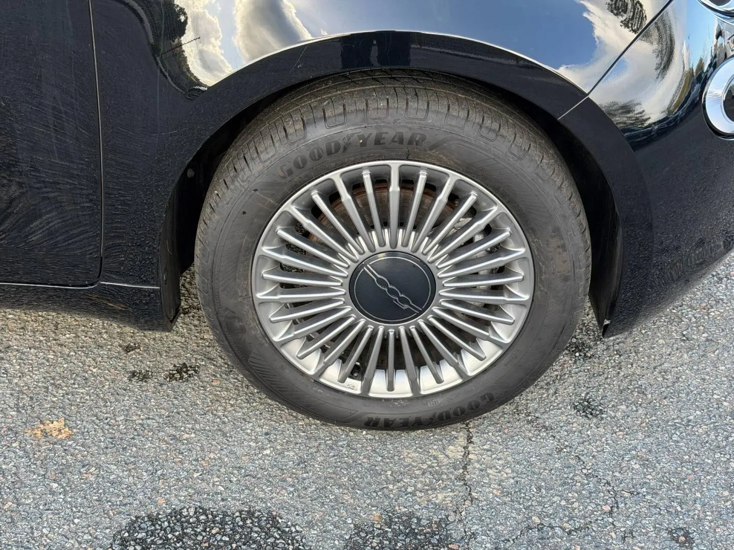 Gros plan sur la roue avant gauche d'une Fiat 500 e 118ch MY24 noire Onyx Black avec jante argentée à rayons fins.