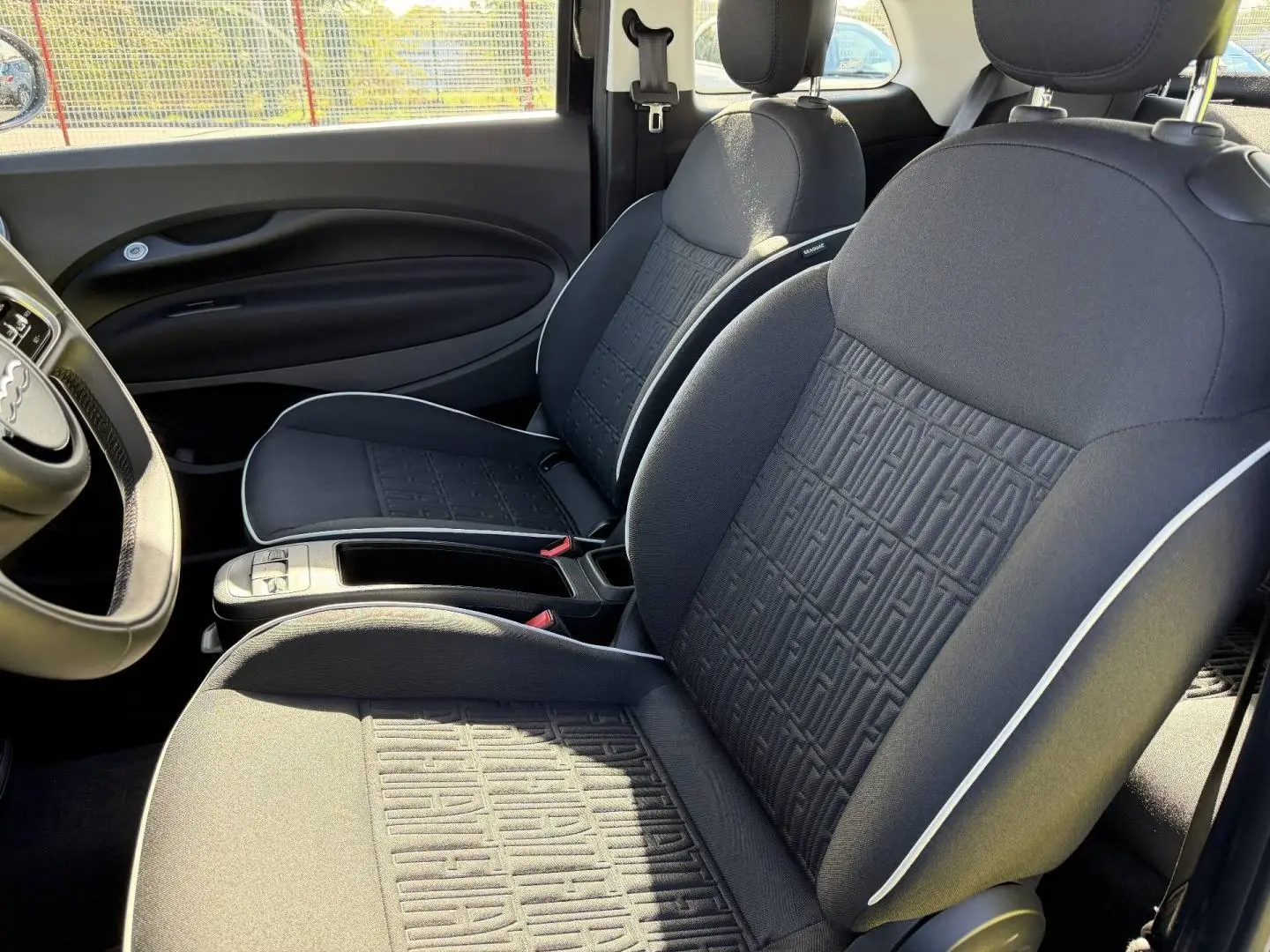 Vue intérieure côté droit de la Fiat 500 e 118ch MY24 avec sièges noirs monogramme Fiat et surpiqûres blanches.