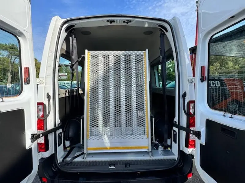 Vue arrière du Renault Master Combi blanc minéral avec portes ouvertes et rampe d'accès TPMR déployée dans le coffre.
