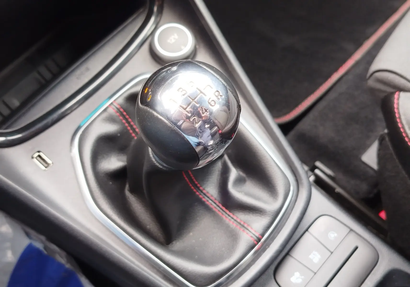 Gros plan sur le levier de vitesses manuel chromé avec coutures rouges dans l'habitacle gris du Ford Puma 2021.
