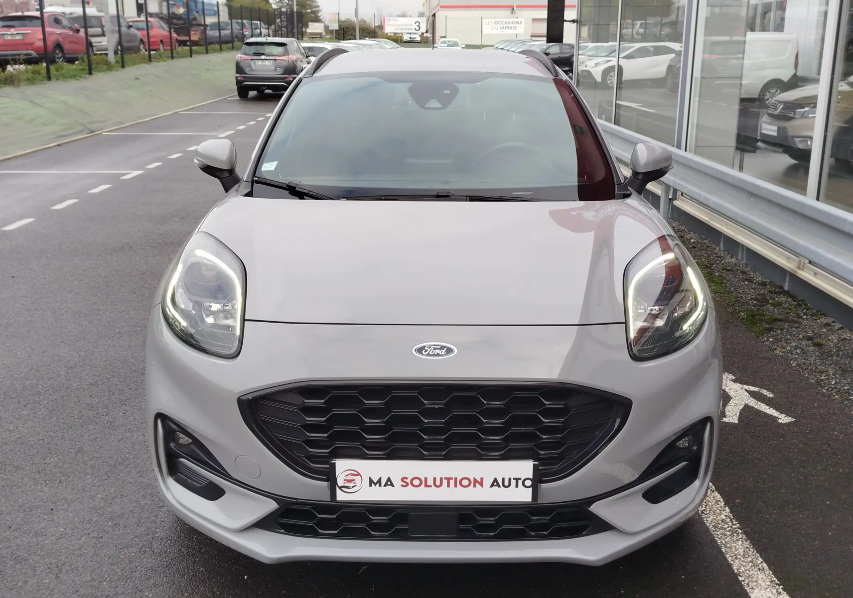 Vue frontale d'une Ford Puma 1.0 EcoBoost 125ch mHEV ST-Line en gris Fashion, avec phares LED allumés.