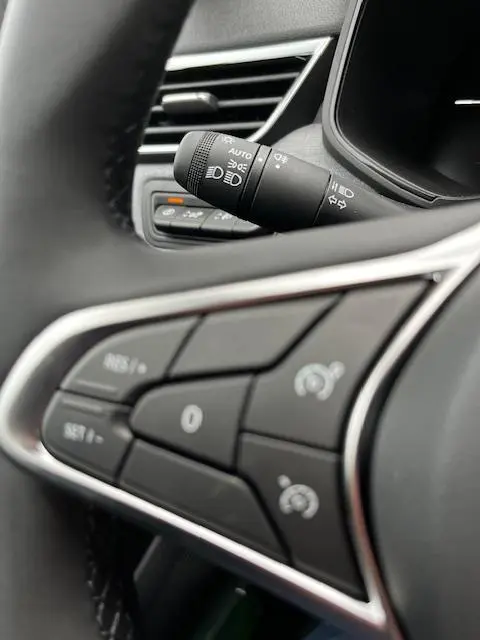 Gros plan sur les commandes au volant et la manette des phares d'une Renault Clio noire Evolution Blue dCi 100, intérieur moderne.