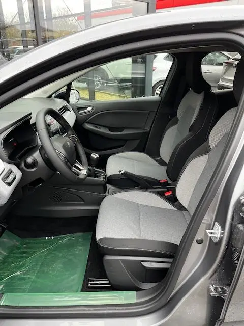 Vue intérieure côté conducteur de la Renault Clio 2025, sièges gris clair avec volant multifonctions en cuir noir.