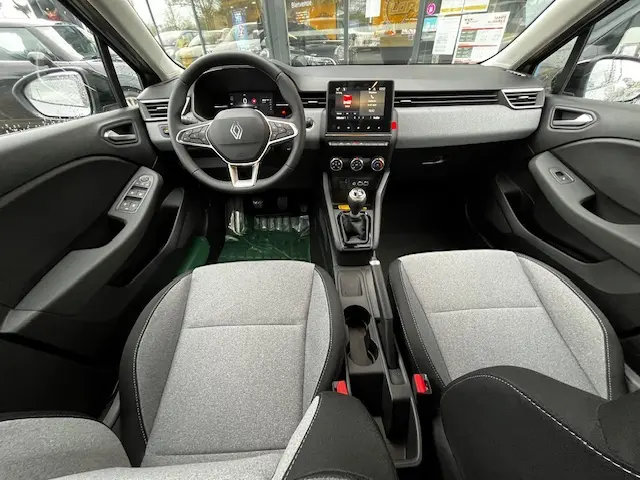 Vue intérieure avant de la Renault Clio noire 2025, avec volant multifonctions, écran tactile central et sièges gris clair.