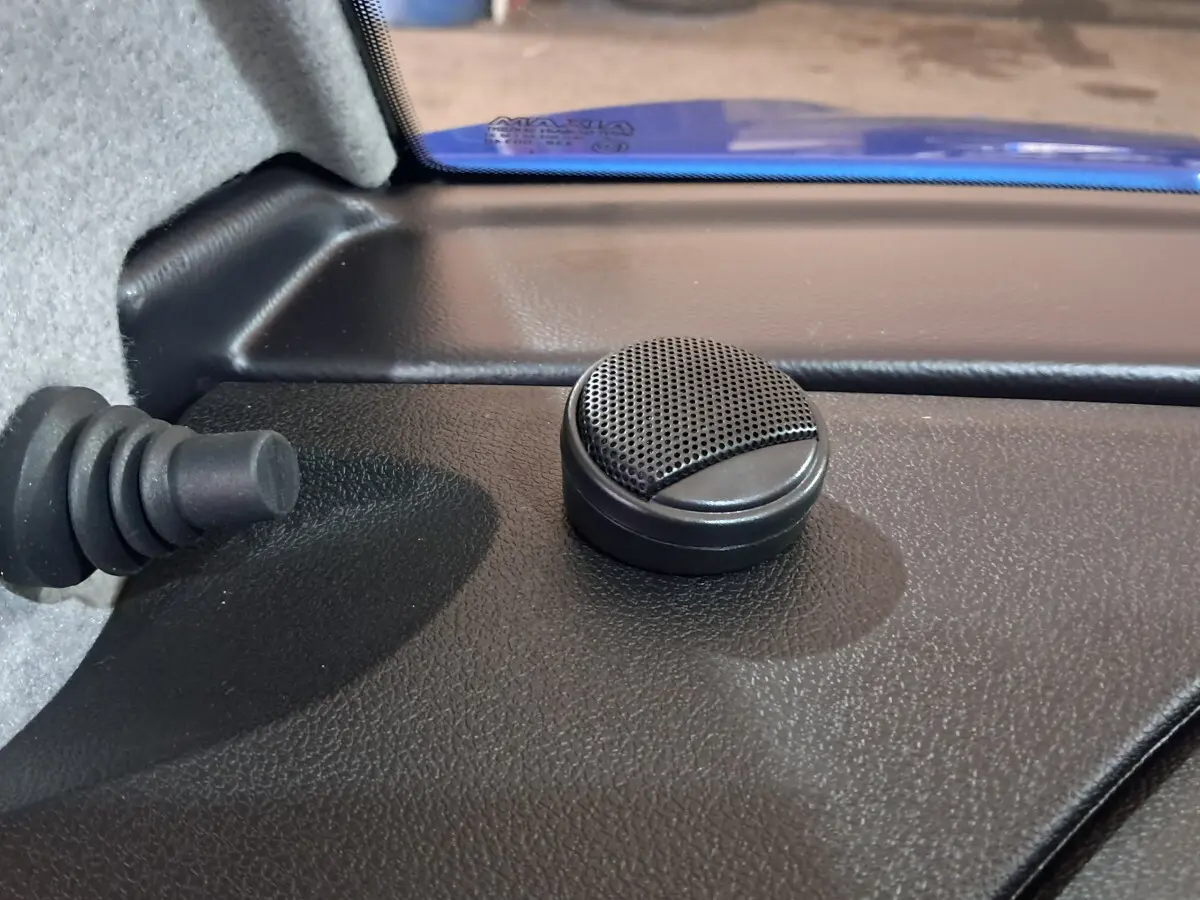 Gros plan sur un haut-parleur rond noir à l'intérieur d'une Aixam Ambition bleu, côté conducteur, près du pare-brise.