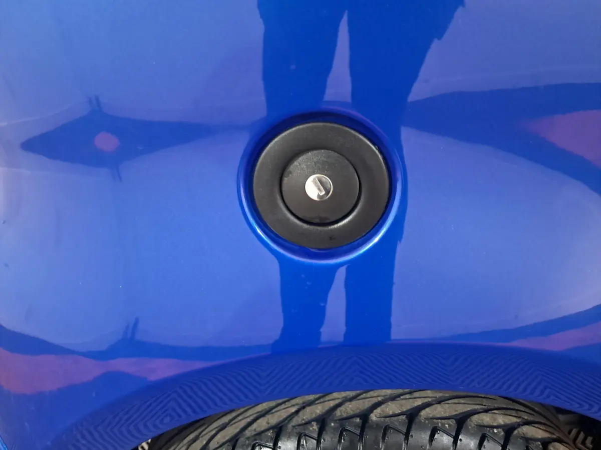 Gros plan sur la serrure de la trappe à carburant d'une Aixam Ambition bleu, avec partie de pneu visible en bas.