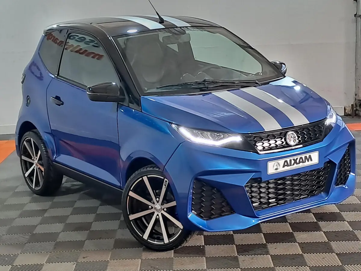 Vue 3/4 avant droite de l'AIXAM AMBITION bleu 2026 avec bandes grises, jantes noires et rétroviseur caméra côté conducteur.