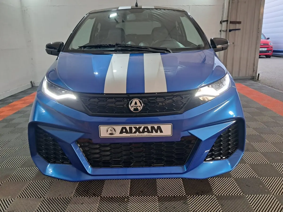 Vue frontale d'une AIXAM Ambition bleue 2026 avec bandes blanches sur le capot et phares allumés.