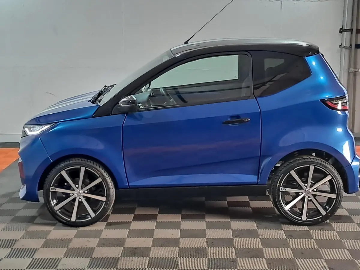 Vue de profil côté gauche de l'AIXAM AMBITION 0.5 CITY GTO bleu avec toit noir et jantes noires à rayons.