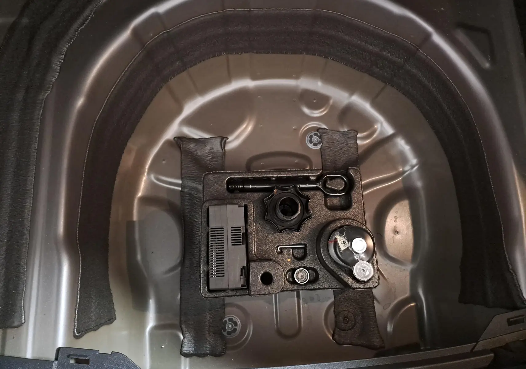 Gros plan sur le rangement sous le coffre du Volkswagen Taigo 1.5 TSI 150 DSG7 R-Line Edition, montrant l’outillage d’origine.