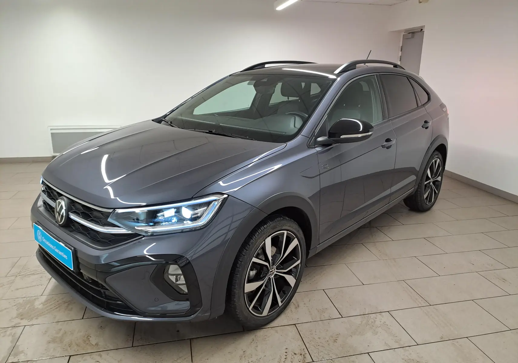 Volkswagen Taigo 1.5 TSI R-Line gris cendré avec toit noir, vue 3/4 avant droit en intérieur showroom.