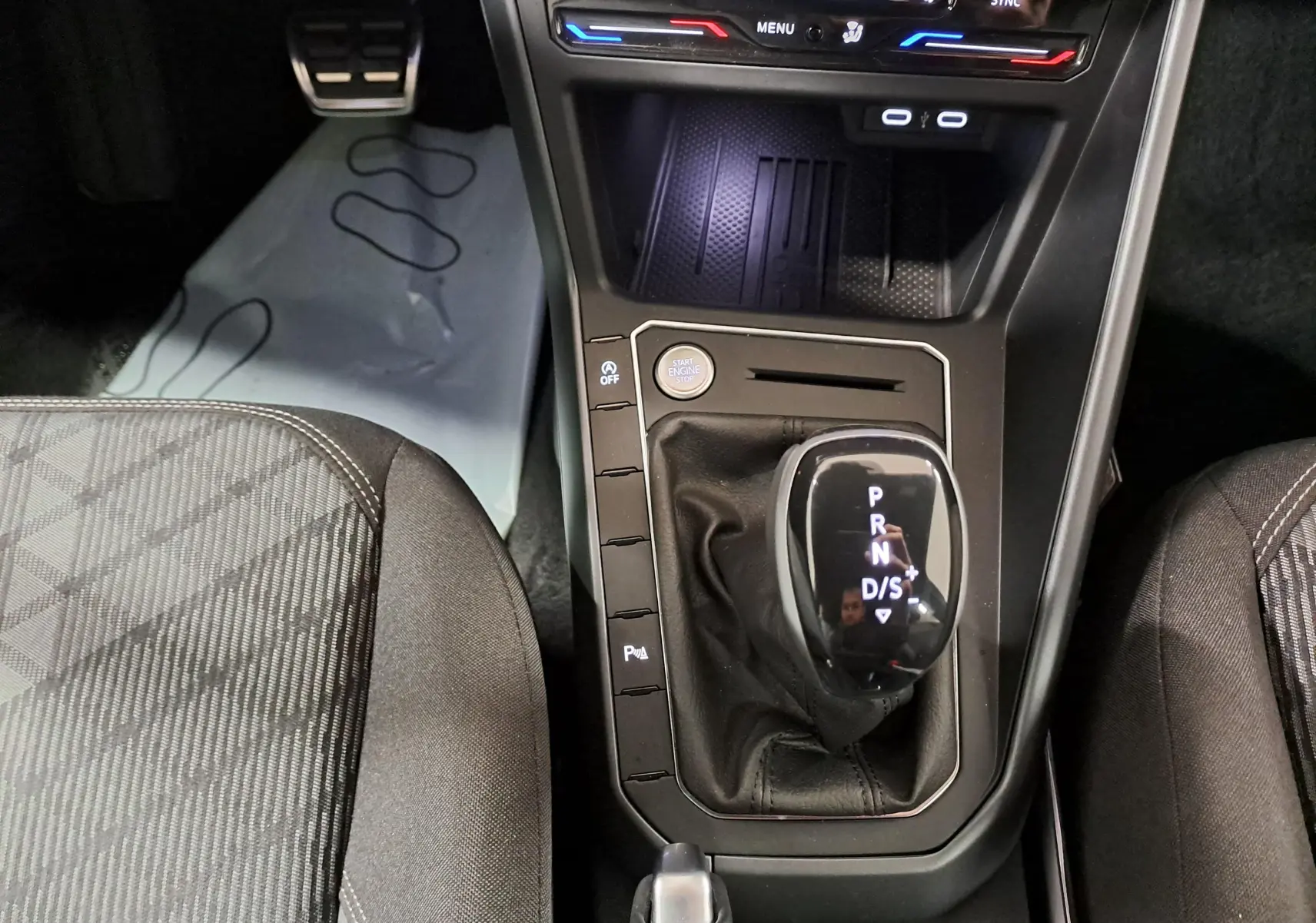 Vue rapprochée de la console centrale du Volkswagen Taigo 1.5 TSI 150 DSG7 R-Line avec levier de vitesses automatique et sièges tissu à motifs.