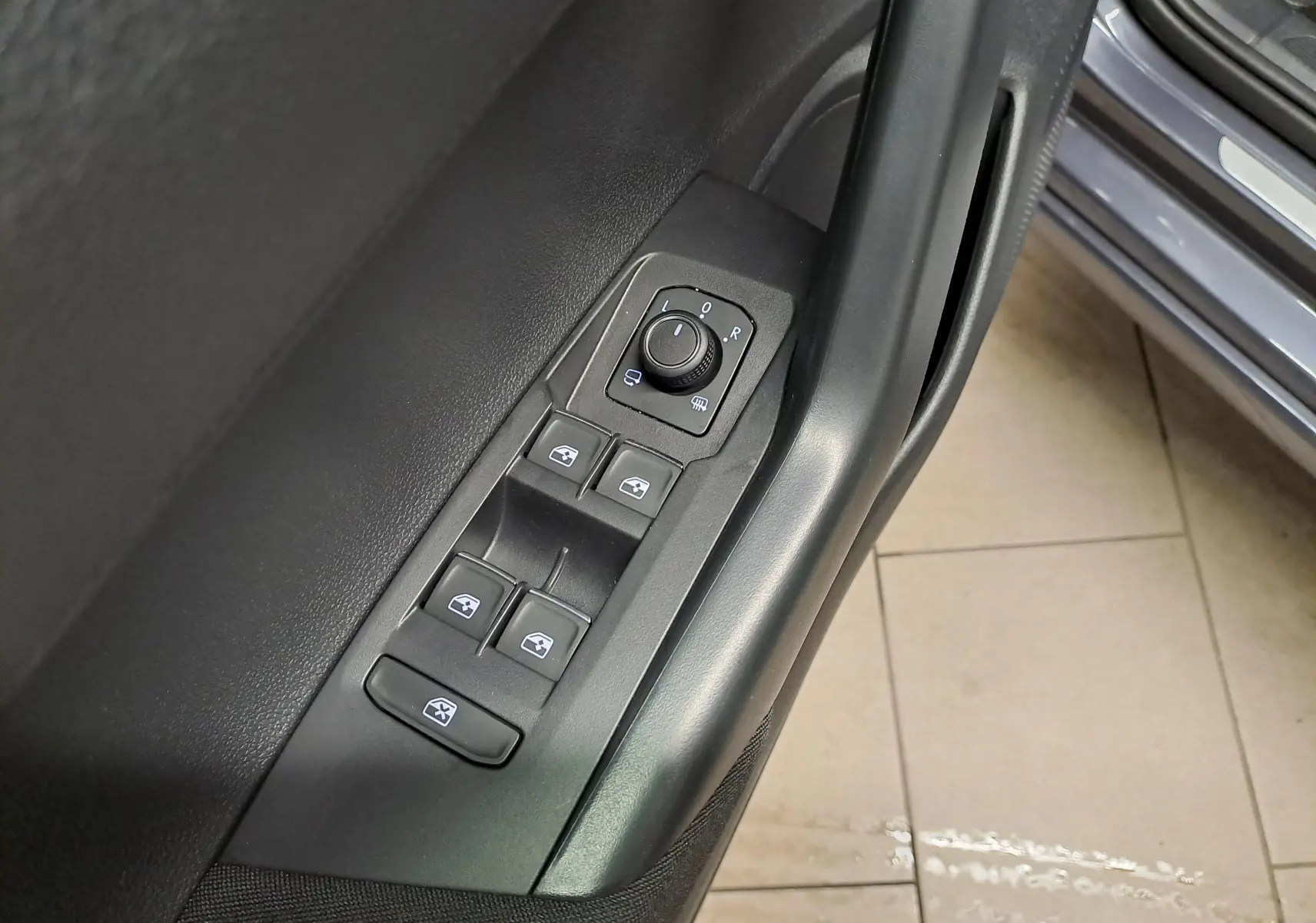 Gros plan sur les commandes de lève-vitres et réglage des rétroviseurs côté conducteur du Volkswagen Taigo gris cendré.