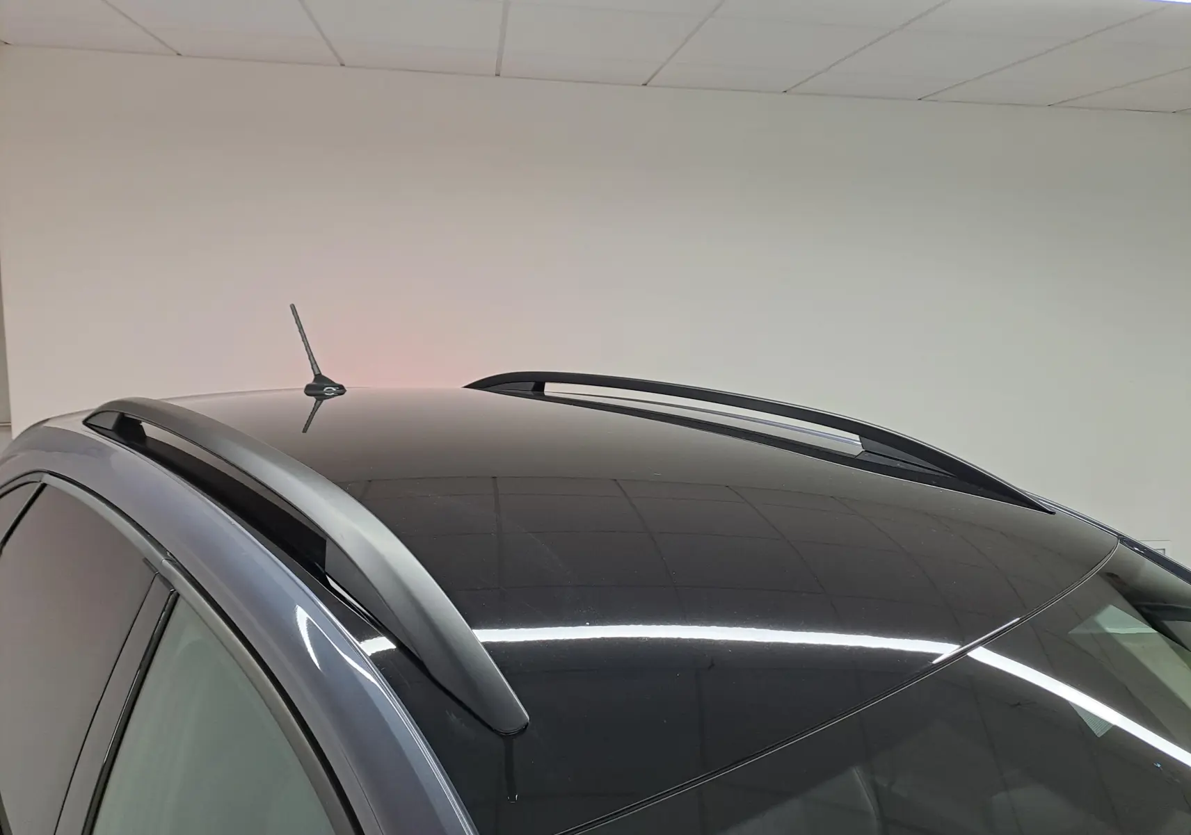 Toit noir brillant avec antenne et barres de toit grises sur Volkswagen Taigo gris cendré, vue partielle côté gauche.