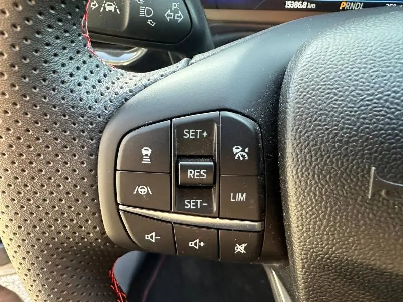 Gros plan sur les commandes au volant perforé avec surpiqûres rouges du Ford Puma 2024 gris Solar Métallisé.