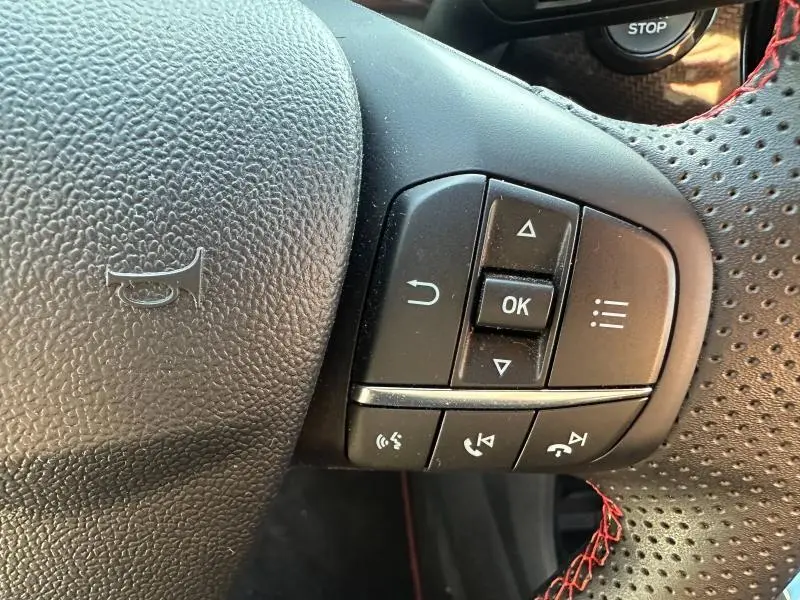 Gros plan sur les commandes multifonctions à droite du volant perforé noir du Ford Puma gris Solar Métallisée 2024.