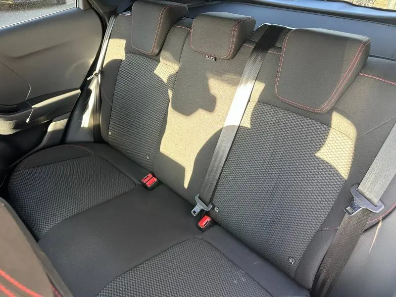 Vue intérieure de la banquette arrière du Ford Puma 2024, tissu noir avec surpiqûres rouges et ceintures de sécurité visibles.