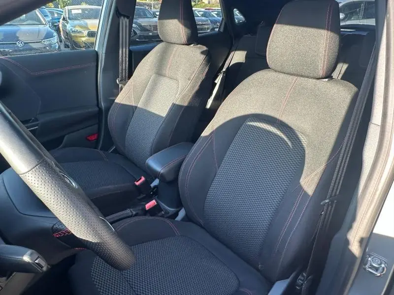 Vue intérieure côté conducteur du Ford Puma 2024, sièges noirs avec surpiqûres rouges et volant en cuir perforé.