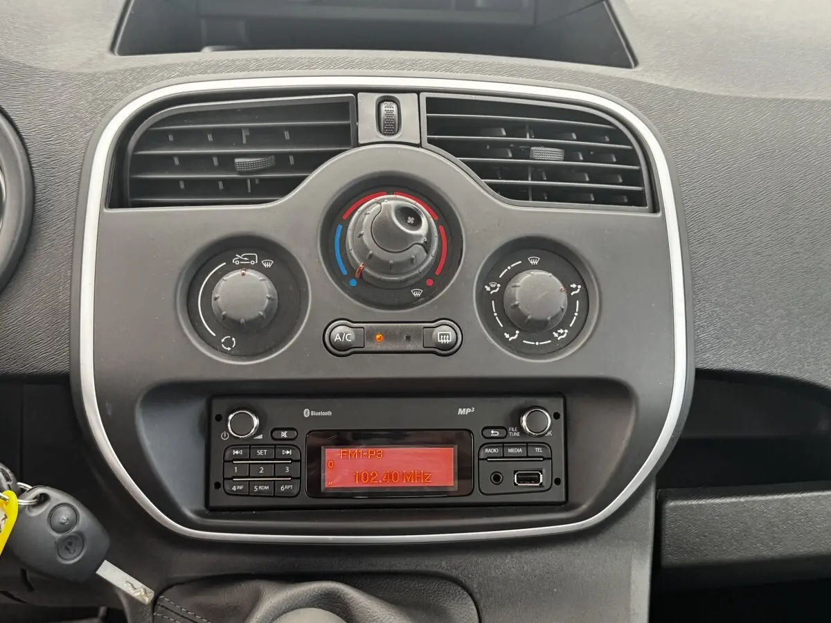 Vue rapprochée du tableau de bord central du Renault Kangoo blanc 2016, avec commandes de climatisation et radio affichant 102,40 MHz.