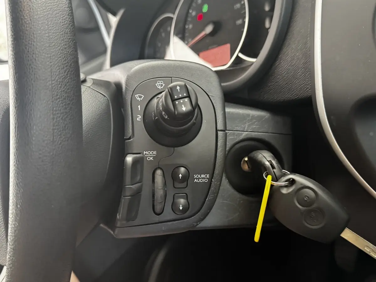 Gros plan sur la commande audio au volant et la clé insérée dans le contact d’un Renault Kangoo Zen blanc de 2016.