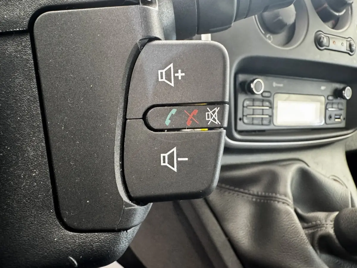 Gros plan sur les commandes au volant noir du Renault Kangoo blanc, avec la console radio en arrière-plan.