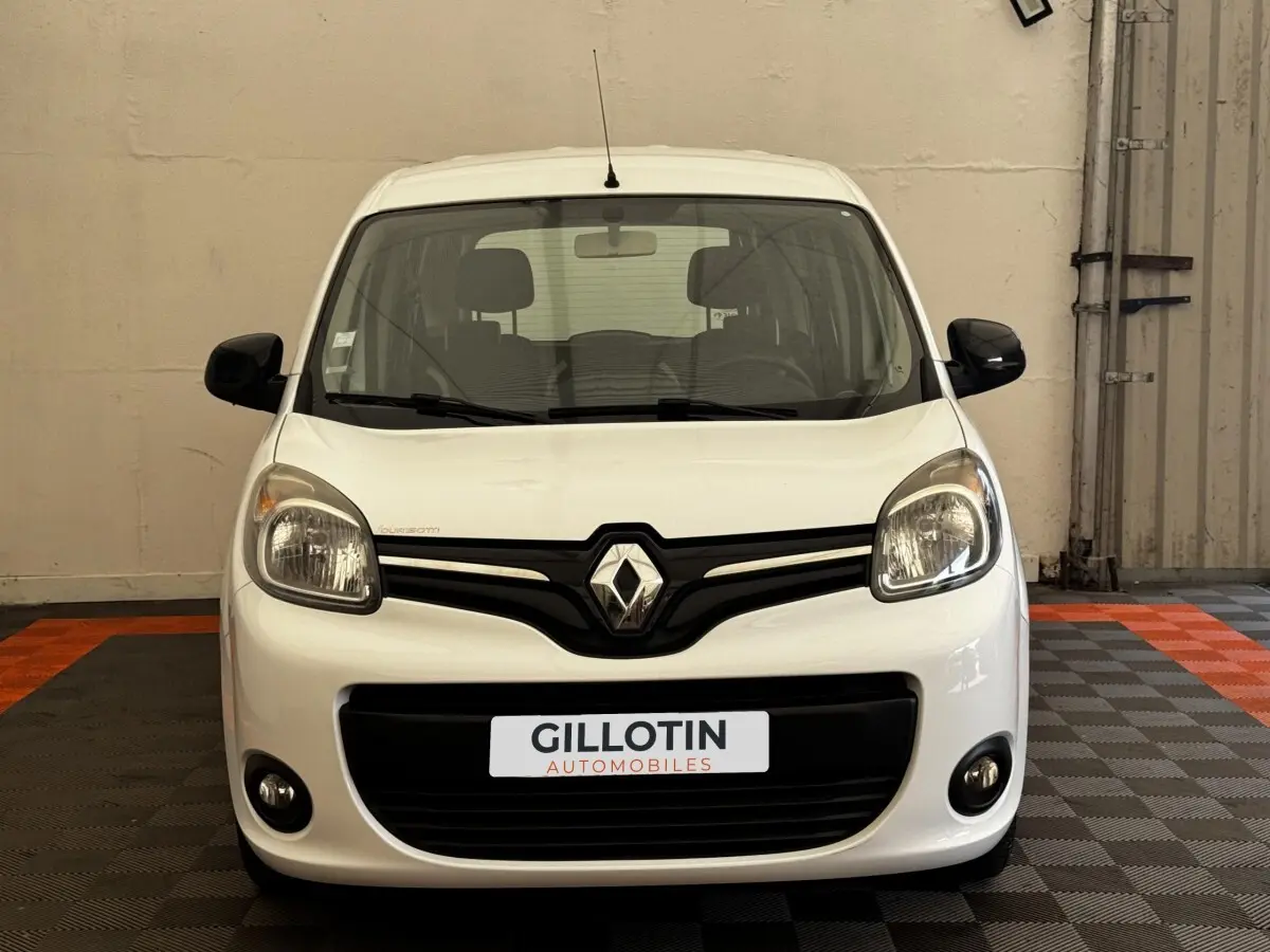 Vue avant d'un Renault Kangoo blanc avec calandre noire et phares arrondis dans un garage.