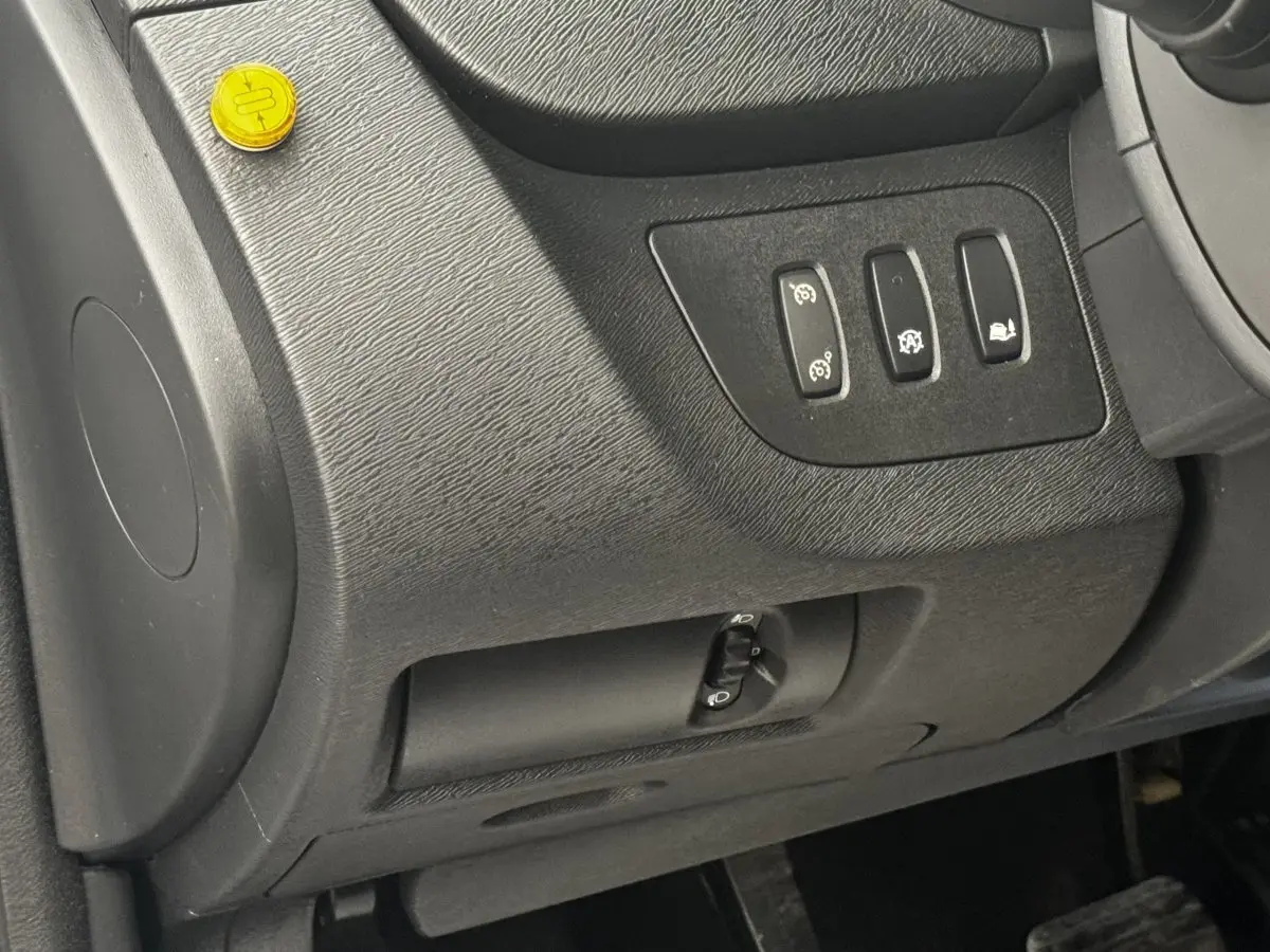 Vue intérieure du tableau de bord côté conducteur du Renault Kangoo blanc, avec commandes des aides à la conduite et réglage des phares.